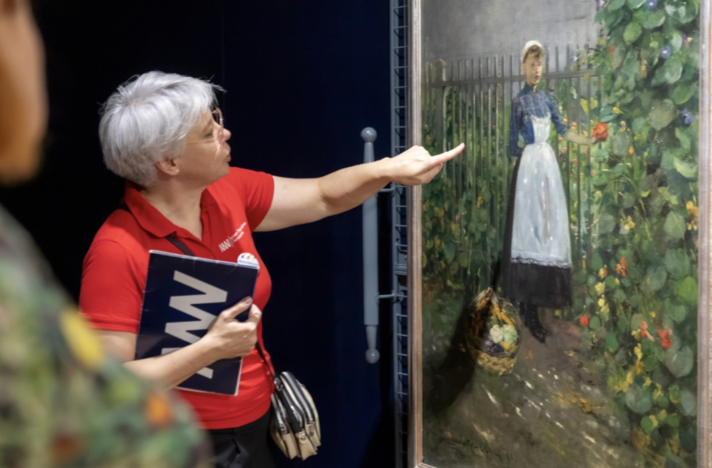 Zdjęcie przedstawia wolontariuszkę Muzeum Narodowego w Warszawie, która opowiada o obrazie Olgi Boznańskiej pod tytułem 