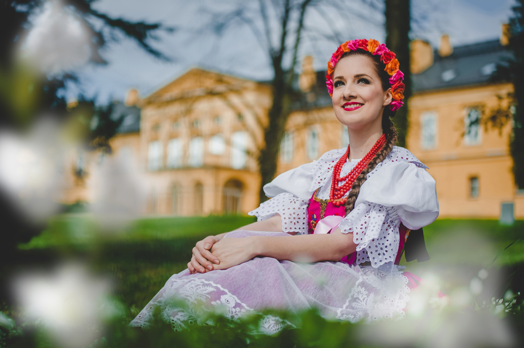 Kobieta w stroju ludowym, w tle pałac - siedziba Zespołu Pieśni i Tańca Śląsk.