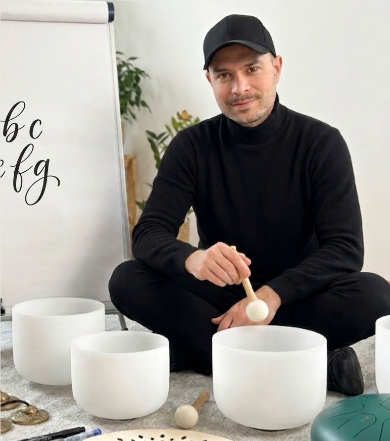 Patryk Martuś ubrany w czarny strój, siedzi na podłodze. W ręku trzyma pałeczkę, przed nim ustawione są białe misy. W tle tablica z wykaligrafowanym napisem.