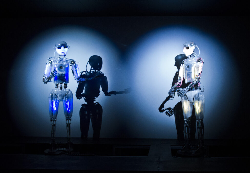 Scena teatru Robotycznego, dwa roboty oświetlone niebieskiem światłem.